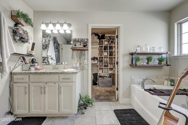 full bath featuring a walk in closet, a garden tub, vanity, and tile patterned floors