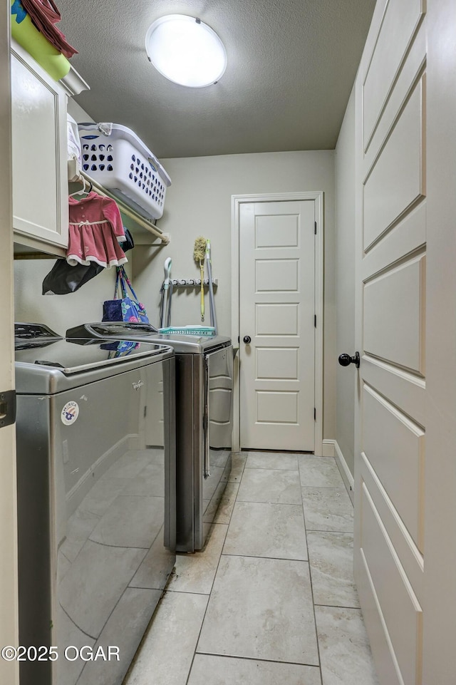 clothes washing area with cabinet space, a textured ceiling, and washing machine and clothes dryer