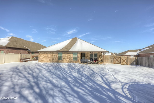 snow covered property featuring a fenced backyard and brick siding