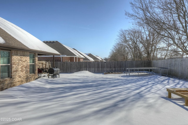 snowy yard featuring a fenced backyard and a trampoline