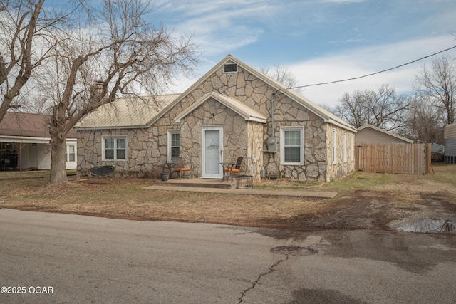 view of front of property with stone siding, a chimney, and fence