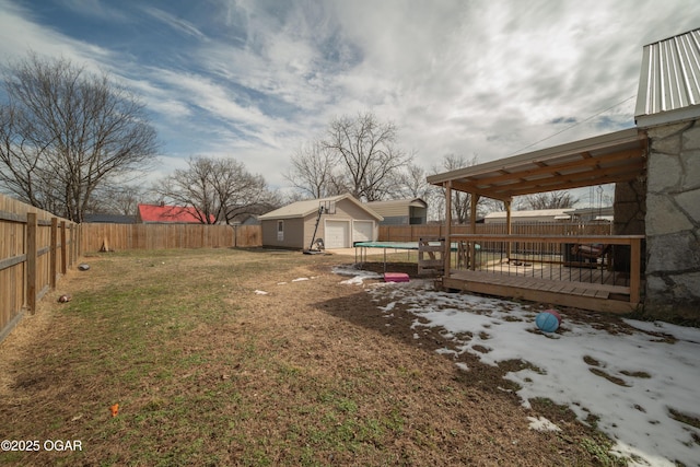 view of yard with a wooden deck, a fenced backyard, an outdoor structure, a detached garage, and a trampoline