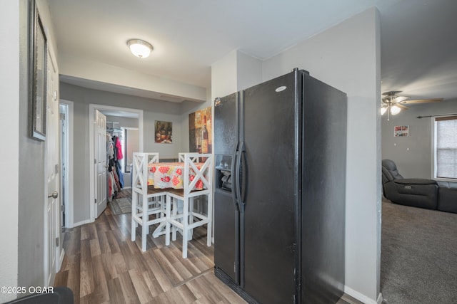 kitchen featuring wood finished floors, baseboards, and black refrigerator with ice dispenser