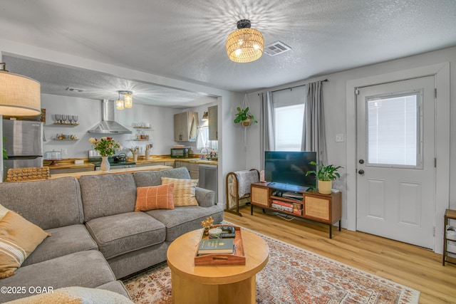 living room featuring visible vents, a textured ceiling, and light wood finished floors