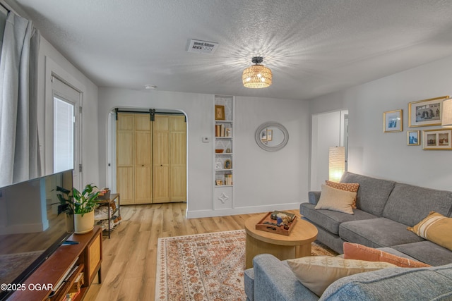 living room with light wood finished floors, baseboards, visible vents, and a textured ceiling