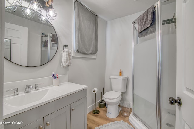 bathroom with baseboards, toilet, wood finished floors, vanity, and a shower stall