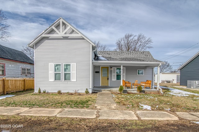 view of front of home with central AC unit, covered porch, a shingled roof, fence, and a front lawn