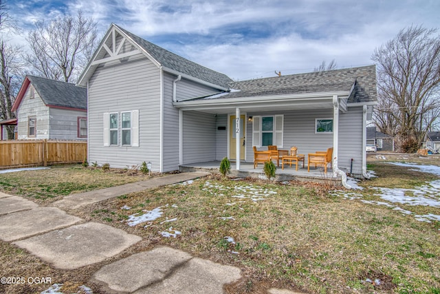 view of front of home featuring a shingled roof, fence, a porch, and a front yard