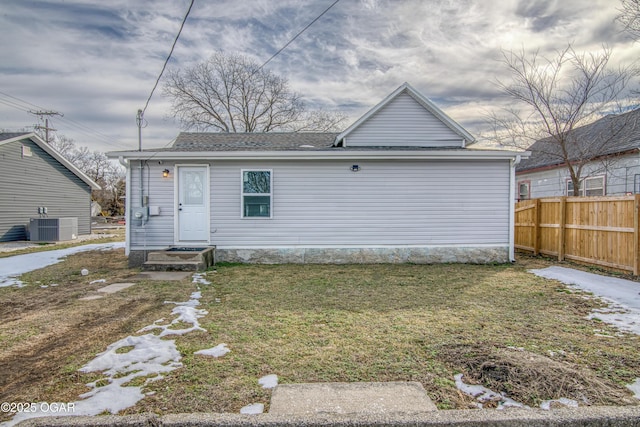 view of front of home with central AC unit, a shingled roof, fence, and a front yard