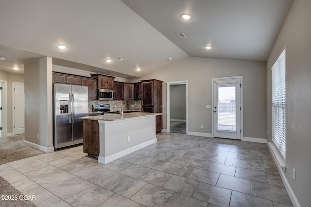 kitchen with visible vents, an island with sink, light stone countertops, vaulted ceiling, and stainless steel appliances