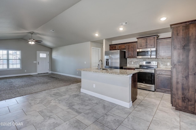 kitchen with dark brown cabinetry, appliances with stainless steel finishes, open floor plan, a kitchen island with sink, and vaulted ceiling