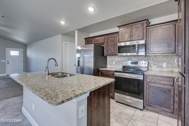 kitchen with tasteful backsplash, an island with sink, appliances with stainless steel finishes, light stone counters, and a sink