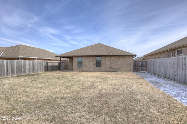 back of house with roof with shingles, brick siding, a lawn, and a fenced backyard