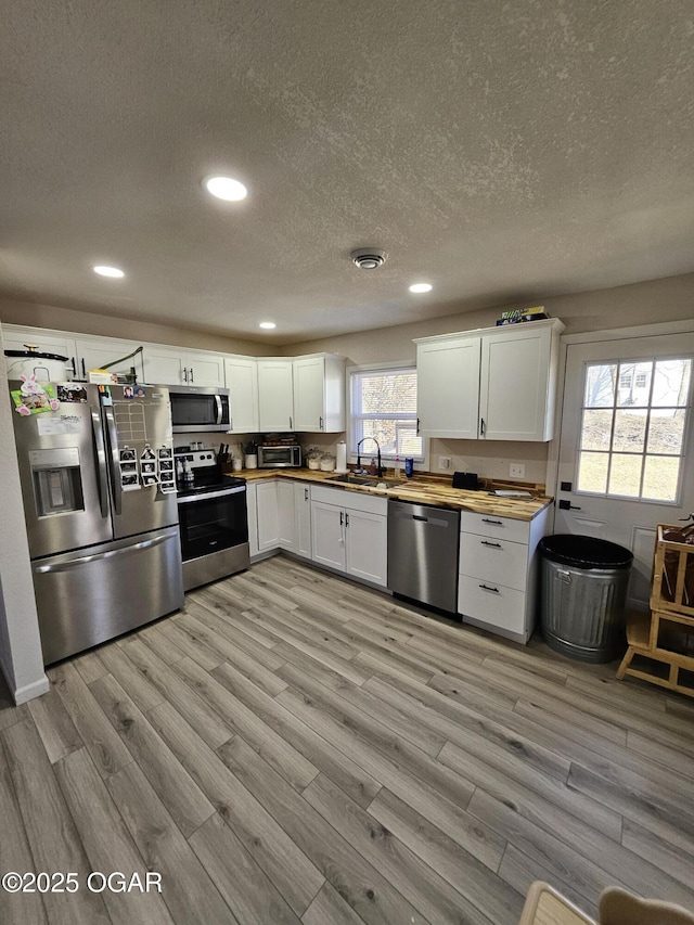 kitchen featuring appliances with stainless steel finishes, light wood-type flooring, wood counters, and white cabinets