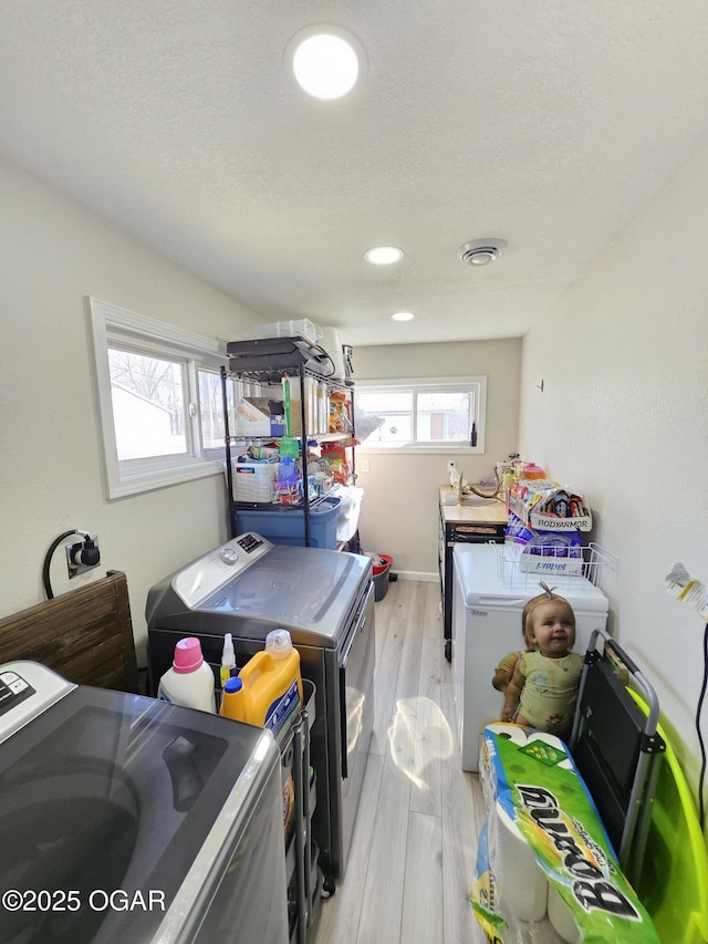 washroom with light wood-type flooring, washing machine and dryer, laundry area, and a textured ceiling