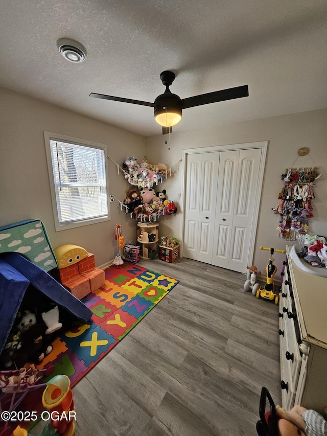 recreation room with a textured ceiling, wood finished floors, visible vents, and a ceiling fan