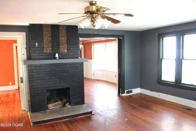 unfurnished living room featuring a brick fireplace, plenty of natural light, visible vents, and wood finished floors