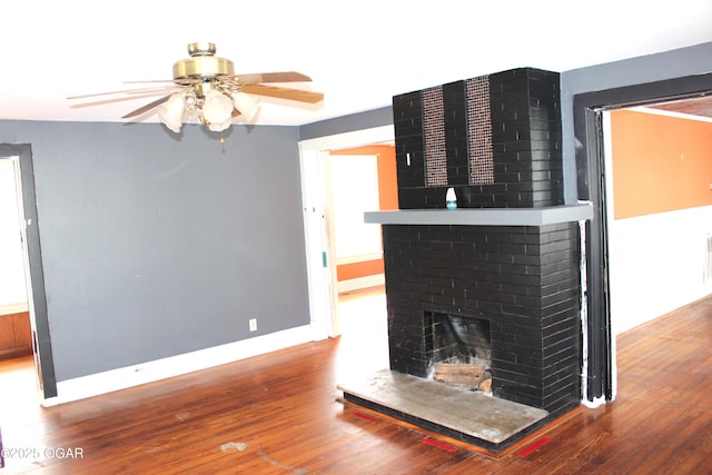 unfurnished living room with a brick fireplace, wood finished floors, a ceiling fan, and baseboards