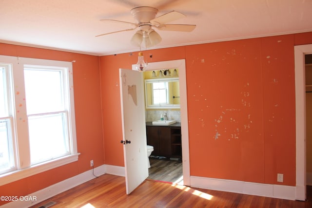 unfurnished room with a ceiling fan, a sink, baseboards, and wood finished floors