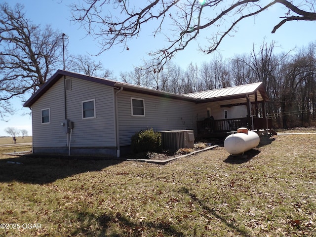 view of side of home with central AC unit, metal roof, and a yard