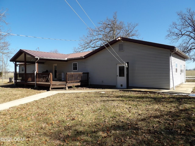 rear view of property featuring metal roof, a deck, and a yard