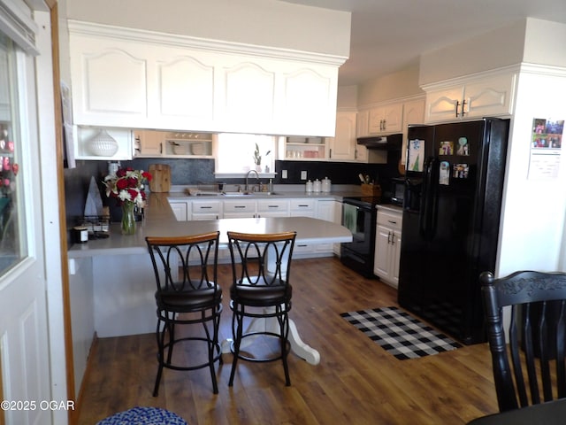 kitchen with a breakfast bar area, white cabinetry, a peninsula, under cabinet range hood, and black appliances