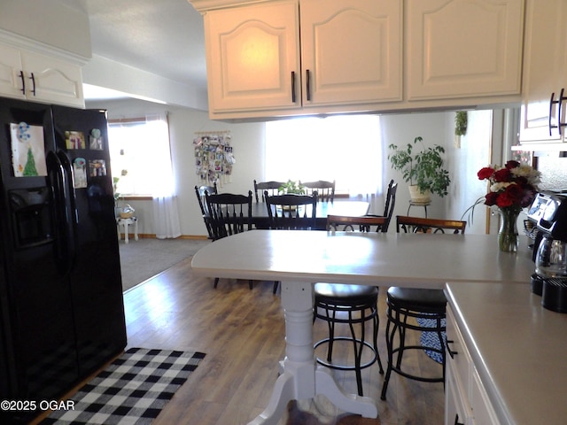 kitchen featuring a breakfast bar, white cabinetry, light countertops, black refrigerator with ice dispenser, and light wood finished floors