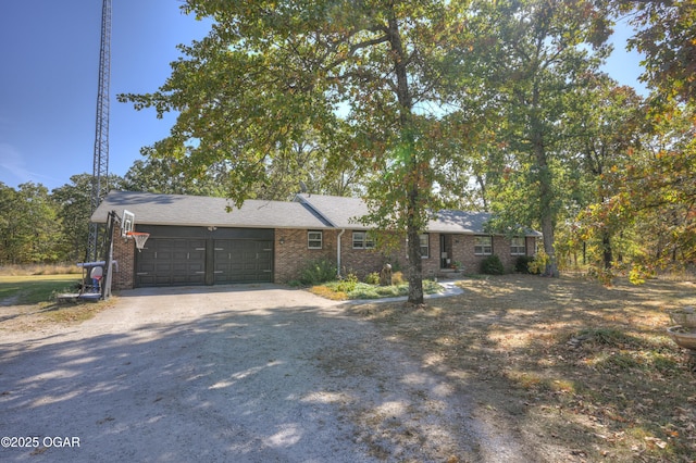 ranch-style home featuring an attached garage, brick siding, and gravel driveway