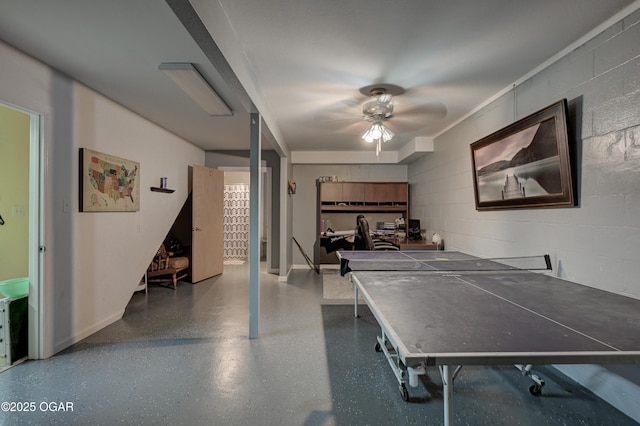 rec room featuring speckled floor, concrete block wall, and a ceiling fan