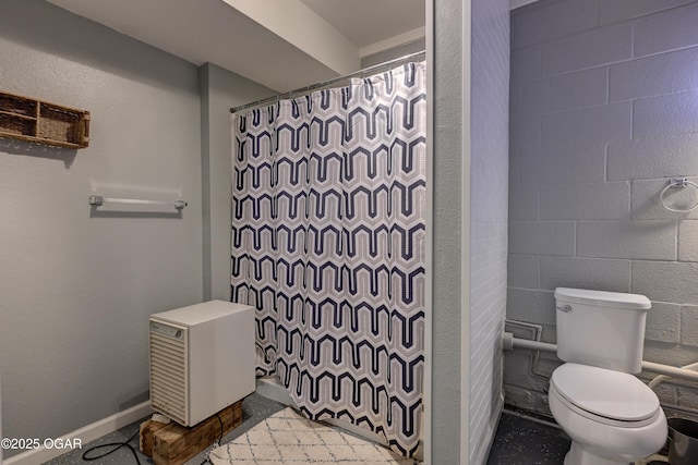 full bathroom with baseboards, curtained shower, toilet, and concrete block wall