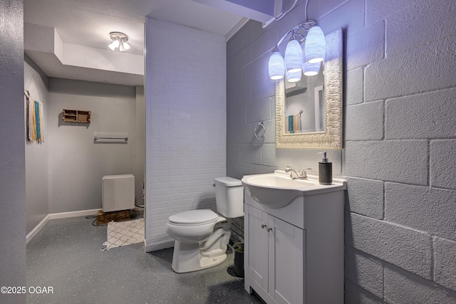 bathroom with toilet, concrete block wall, baseboards, and vanity