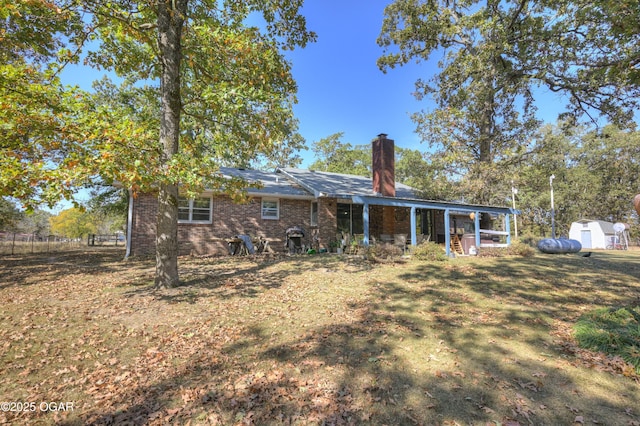 back of property with an outbuilding, brick siding, a chimney, a lawn, and a storage shed