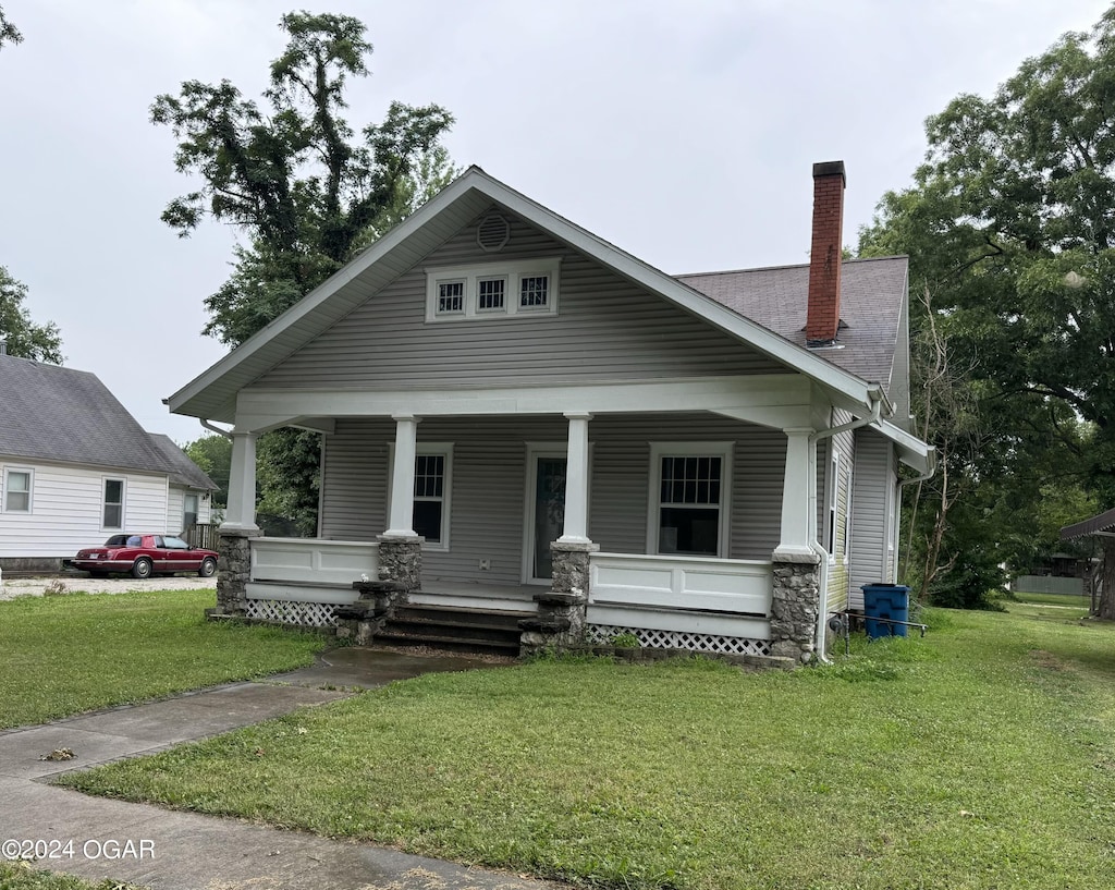 707 Grand St, Lamar, MO 64759 - view of front of property with covered porch, a front lawn, a chimney, and a shingled roof