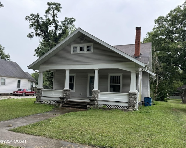 view of front of property with covered porch, a front lawn, a chimney, and a shingled roof