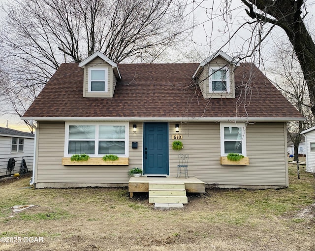 cape cod home featuring a shingled roof and a front yard