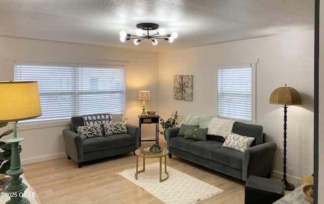 living area with an inviting chandelier, light wood-style flooring, a textured ceiling, and a wealth of natural light