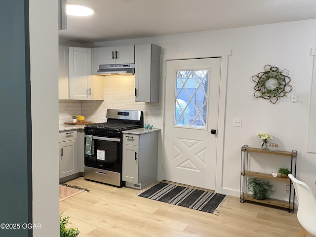 kitchen with under cabinet range hood, light wood-style floors, light stone countertops, stainless steel gas stove, and tasteful backsplash