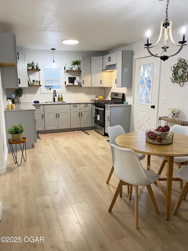 kitchen with light wood finished floors, open shelves, gray cabinetry, gas stove, and a sink