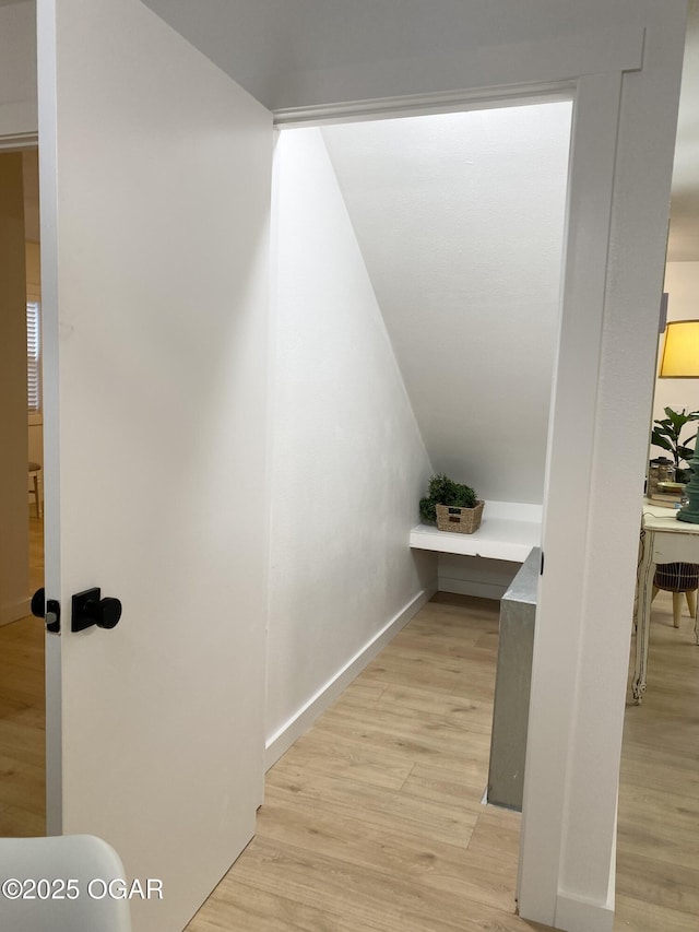 corridor with vaulted ceiling, light wood finished floors, and baseboards