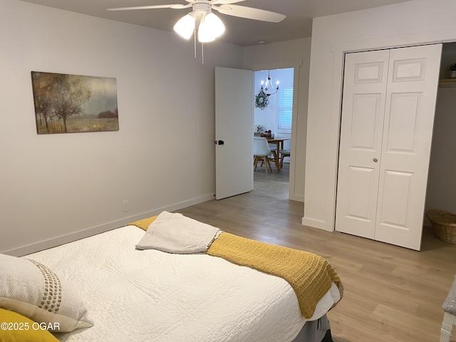 bedroom with a closet, baseboards, light wood finished floors, and ceiling fan with notable chandelier