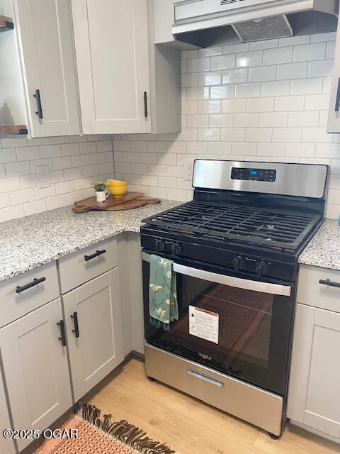 kitchen with under cabinet range hood, stainless steel gas range, light wood-type flooring, backsplash, and light stone countertops