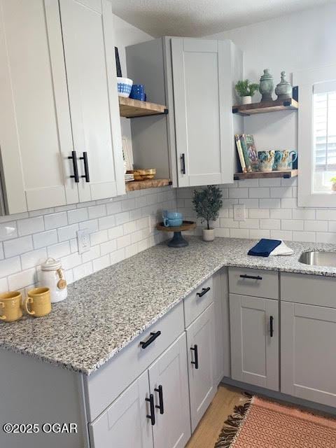 kitchen with light wood-style floors, light stone counters, open shelves, and decorative backsplash