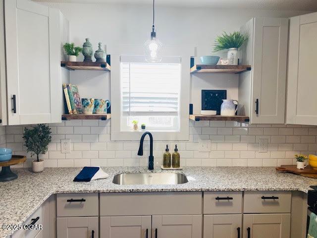 kitchen featuring light stone counters, decorative light fixtures, a sink, open shelves, and backsplash