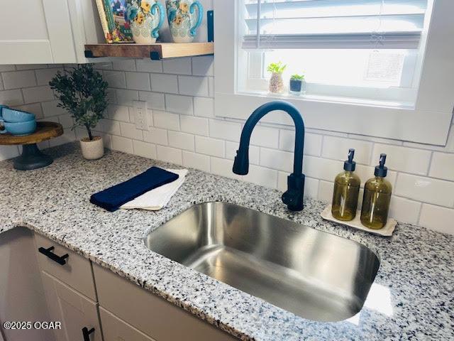 interior details with tasteful backsplash, a sink, light stone countertops, and white cabinets