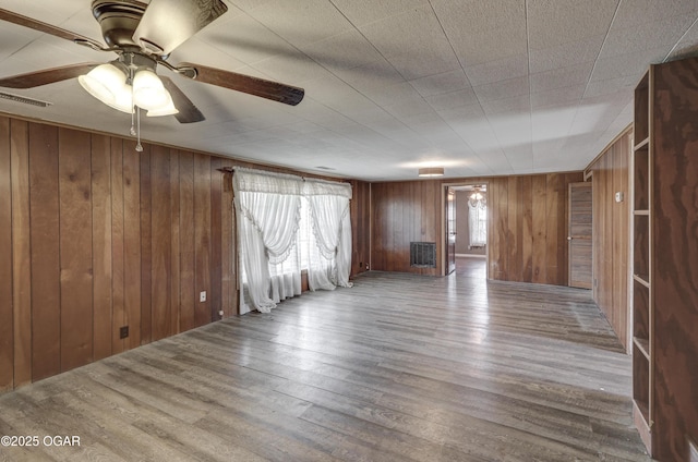 empty room featuring visible vents, ceiling fan, wooden walls, and wood finished floors