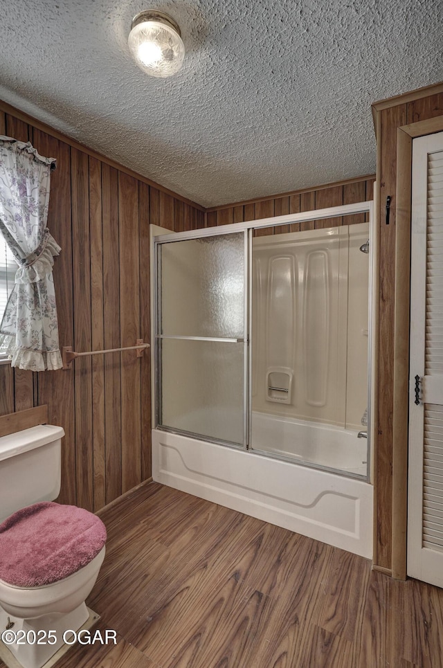 bathroom with combined bath / shower with glass door, wood walls, wood finished floors, and toilet