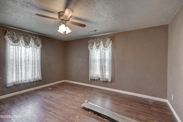 unfurnished room featuring a textured wall, wood finished floors, visible vents, and baseboards