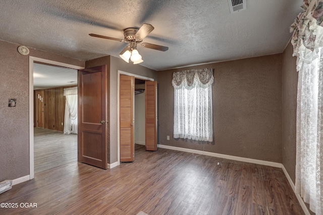 unfurnished bedroom with a textured wall, a closet, wood finished floors, and visible vents