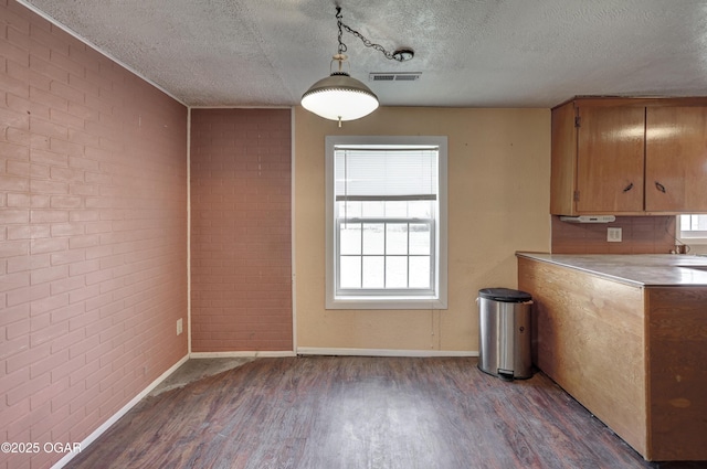 unfurnished dining area with baseboards, visible vents, brick wall, wood finished floors, and a textured ceiling