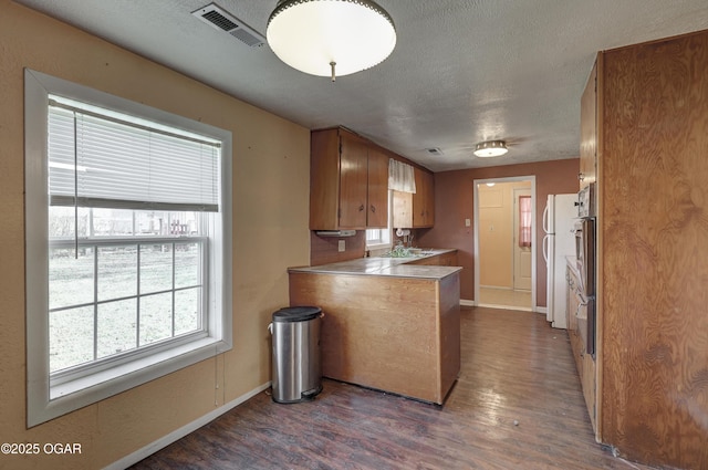 kitchen featuring visible vents, brown cabinetry, dark wood-style floors, a peninsula, and a textured ceiling